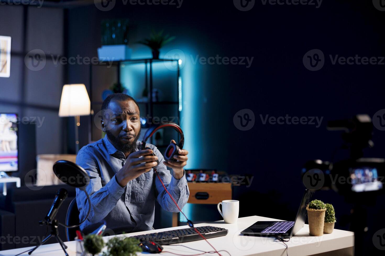 Internet show host holding pair of expensive headphones in hands, doing giveaway for loyal viewers from his home studio. Content creator hosting online contest for fans with audio tech as prize photo