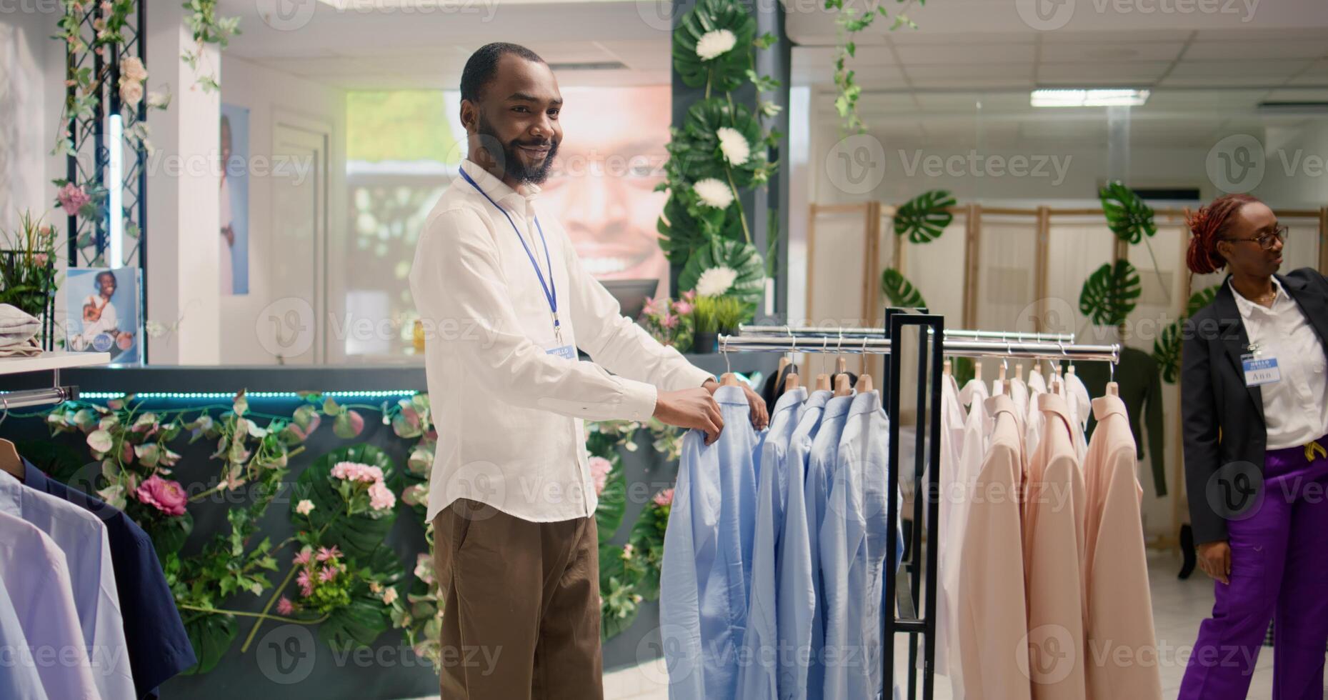 Smiling retail assistant arranging clothes in mall clothing store with fast fashion attire following the latest trends. Cheerful worker organizing assortment of elegant men blazers in fashion boutique photo