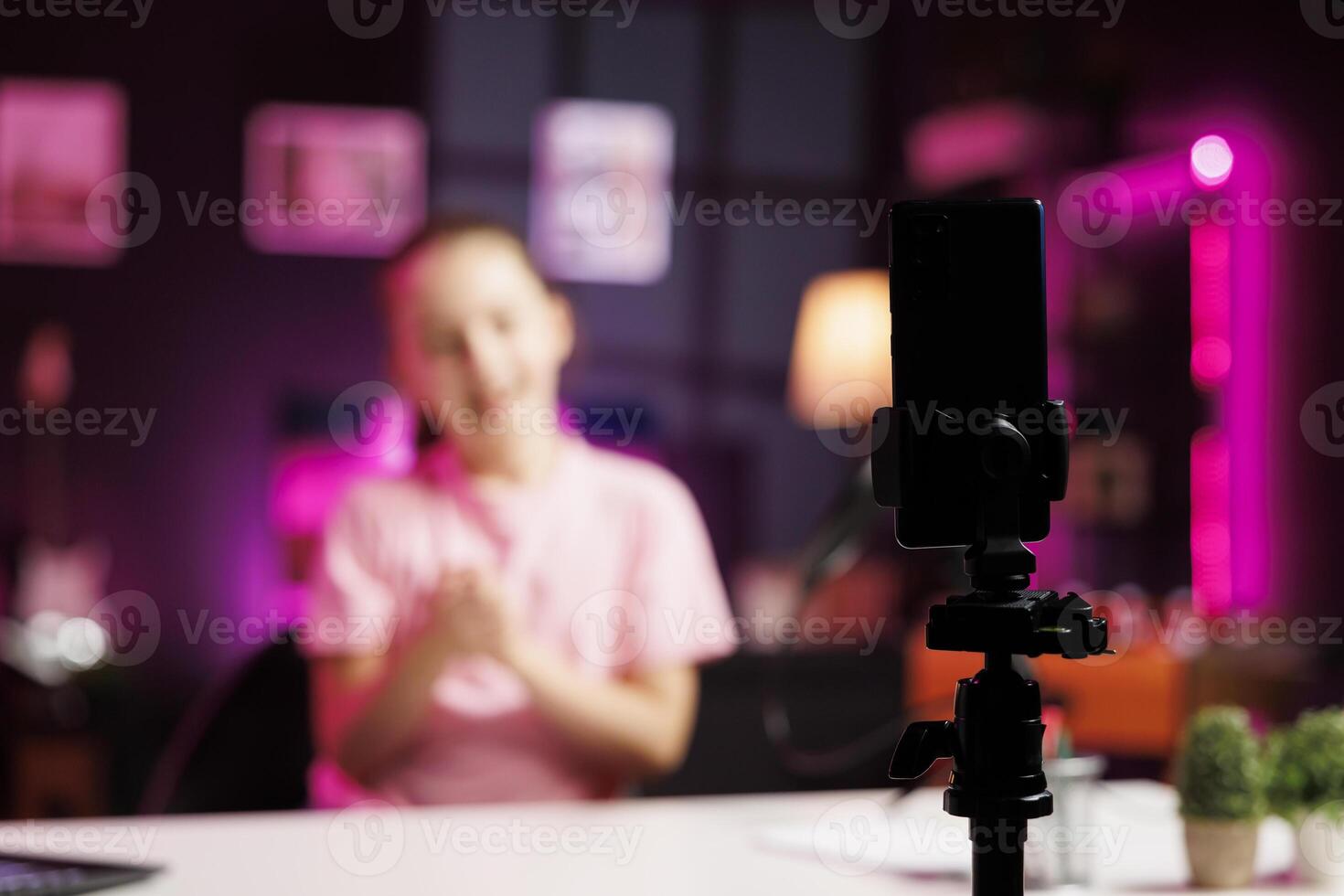 Close up shot of mobile phone on tripod stabilizer used by child to film room tour inside home studio. Focus on phone recording gen Z influencer in blurry background doing video presenting apartment photo