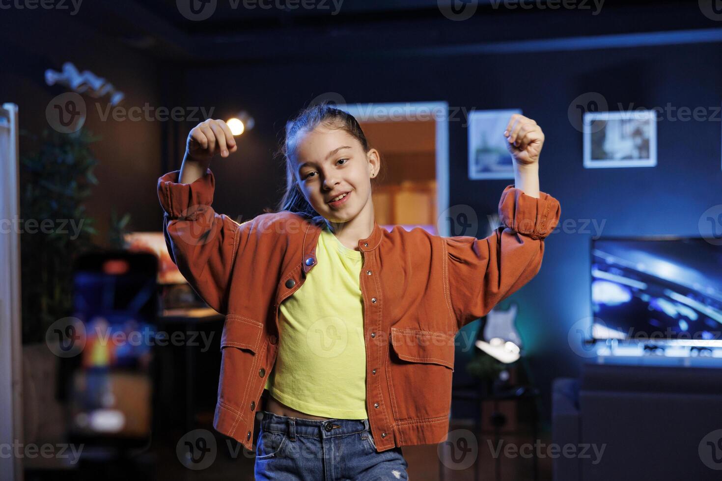 Entertaining kid in dimly lit personal studio joins viral dance craze, recording family friendly video for children audience. Small girl in her apartment does latest internet dancing challenge photo
