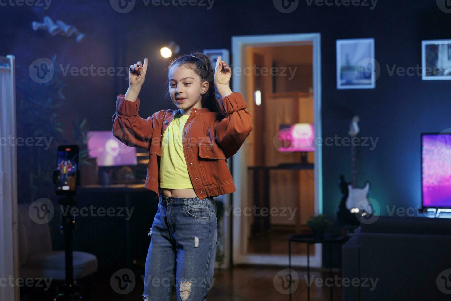 Child takes part in viral dance trend after seeing favorite celebrities doing it, filming video with smartphone on tripod stabilizer. Young media star does trendy dancing challenge, records with phone photo