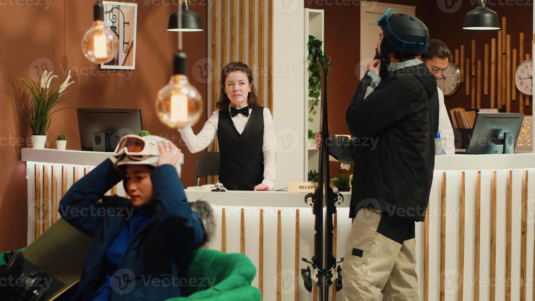 Tourist asking staff for slope direction after arriving at alpine skiing resort, receptionist greeting winter sport enthusiast in lobby. Young man carrying skis and protective gear to do sliding. photo