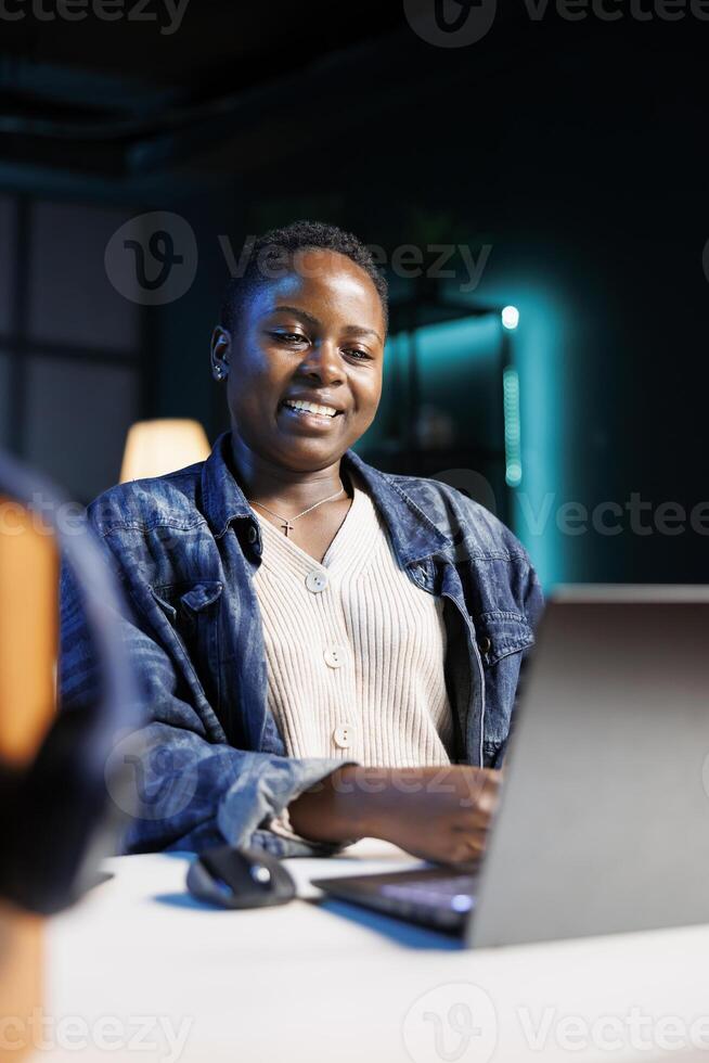 Close-up of smiling female freelancer diligently working from home, browsing the internet. African american woman typing away on her digital laptop, engaged in online remote work. photo