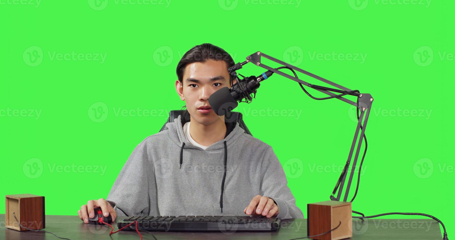 Asian guy does playtime livestream while sitting at workstation and playing online combat video games with his friends. Young man uses microphone to record live broadcast on his desktop pc. photo