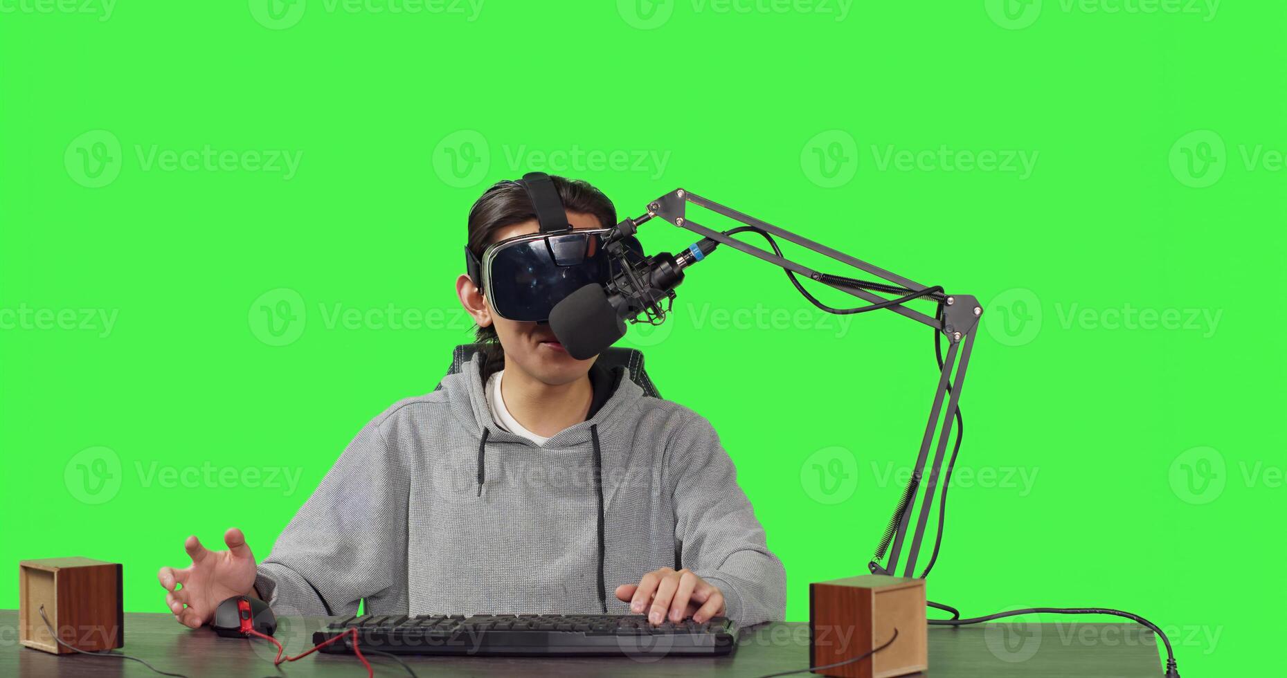 Video blogger streaming live gameplay at workstation, playing online competition with virtual reality headgear. Asian person broadcasting videogames stream, content creator on greenscreen. photo