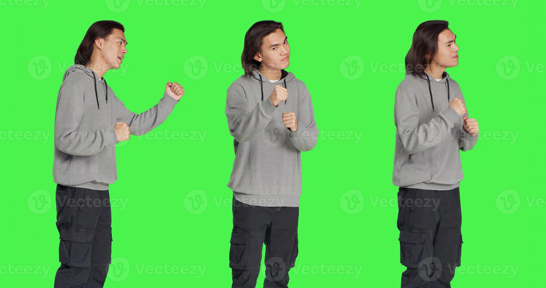 Young man throwing punches in the air, being violent and aggressive in studio. Asian person starting fight with fists, being furious and mad, dangerous behavior on greenscreen. photo