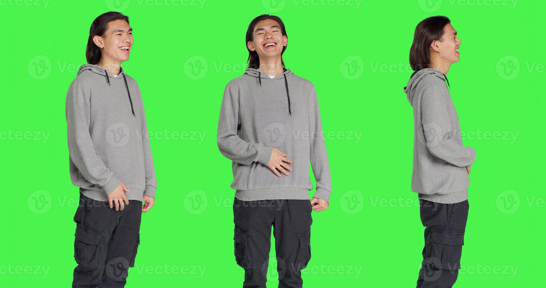 Positive man laughing on camera, posing feeling cheerful against greenscreen backdrop. Asian person smiling in studio, expressing amusing funny gestures, relaxed optimistic guy. photo
