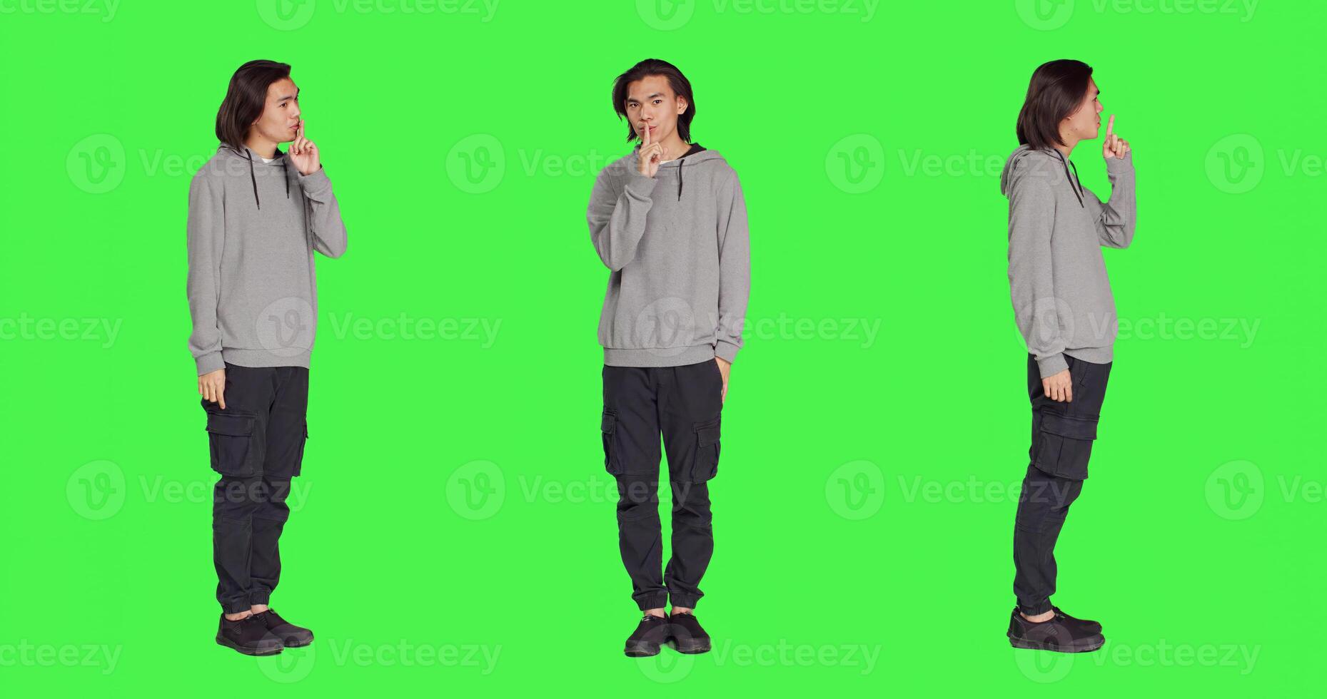 Adult doing hush secret sign over greenscreen, expressing secrecy symbol with finger over lips. Young person showing mute silence gesture , being private in studio with full body backdrop. photo