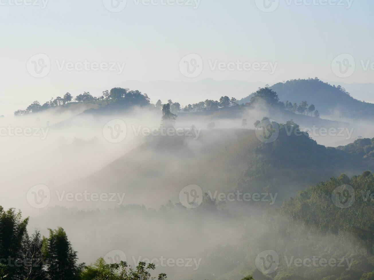 The mist flows through the mountain forest, Sun shining into tropical forest, Mist drifts through mountain ridges in the morning, slow floating fog blowing cover on the top of mountain photo