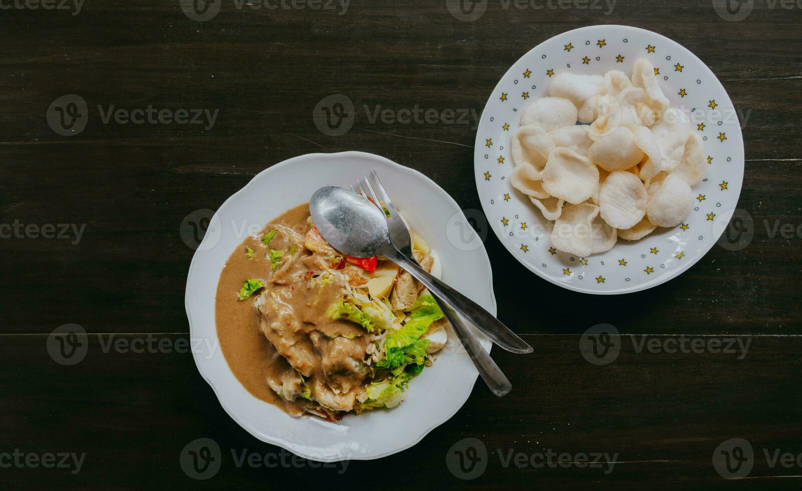 Top view of Javanese vegetable salad with peanut sauce gado-gado served with egg and shrimp cracker. Black wooden background. photo