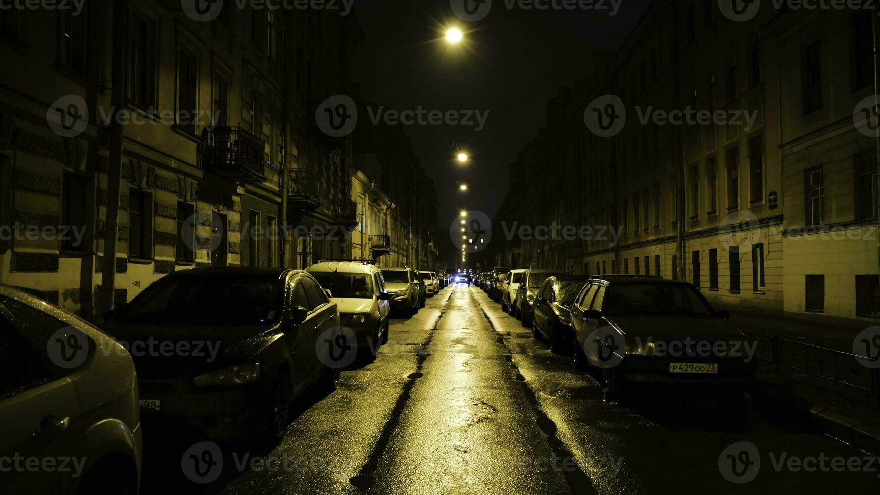 European street in light of yellow lanterns at night with cars in Parking. Concept. Straight beautiful street with residential buildings and parked cars lit by yellow lanterns at night photo