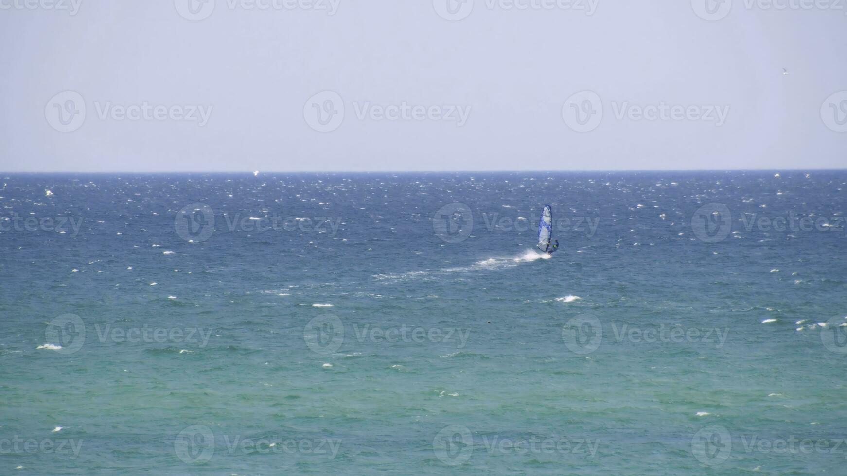 Windsurfer riding the waves in the sea. Shot. Windsurfer in the sea, man on windsurf conquering the waves, enjoying extreme sport, active lifestyle, happy summer vacation photo