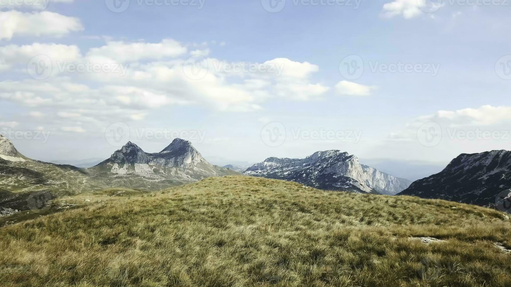 Top view of mountain panorama against blue sky. Stock. Rocky peaks of mountains with cover of grass at foothills create beautiful landscape photo