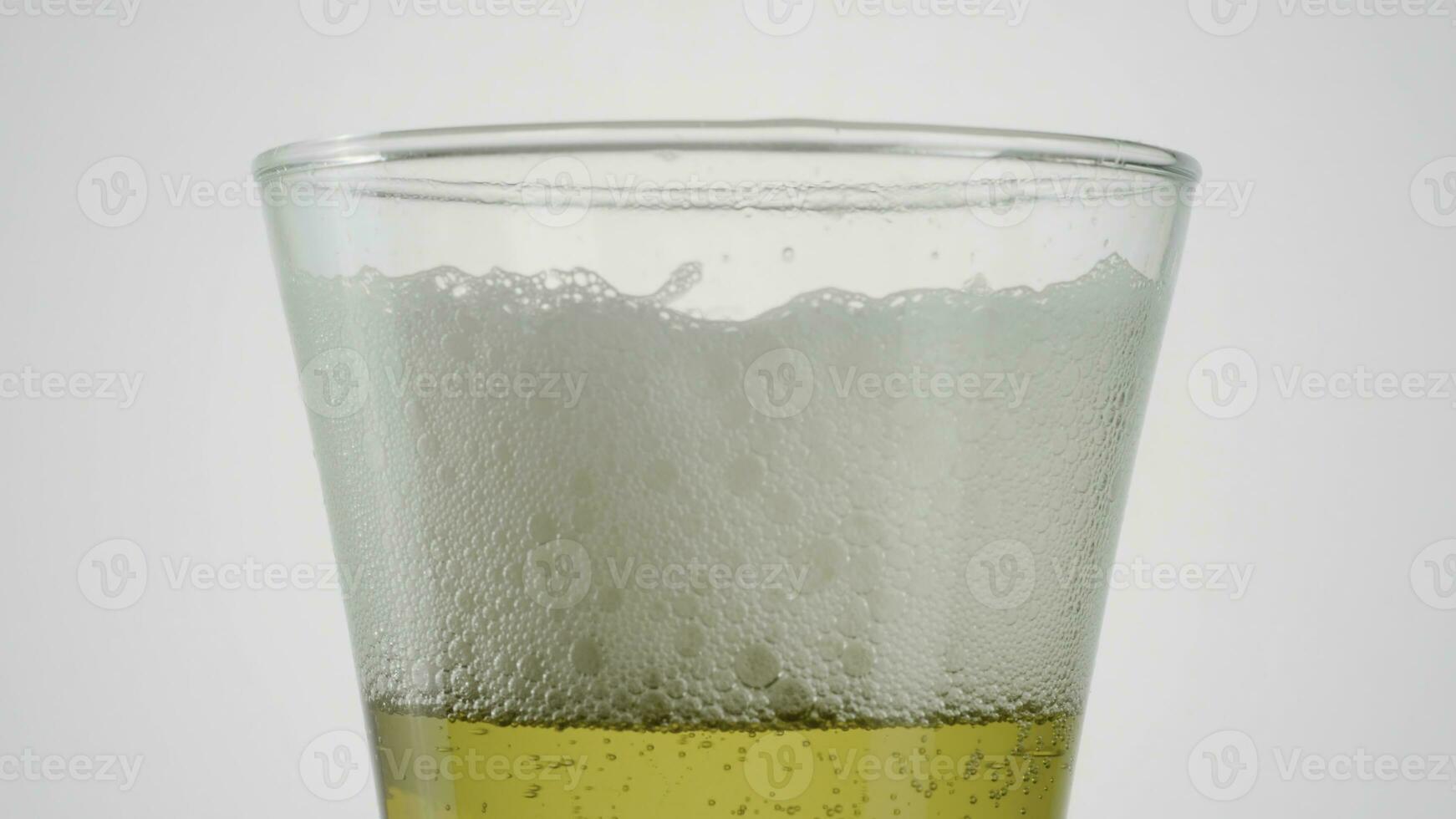 Close-up of beer in clear glass on white background. Action. Beer in glass with disappearing foam on isolated background. Foam in beer slowly disappears photo