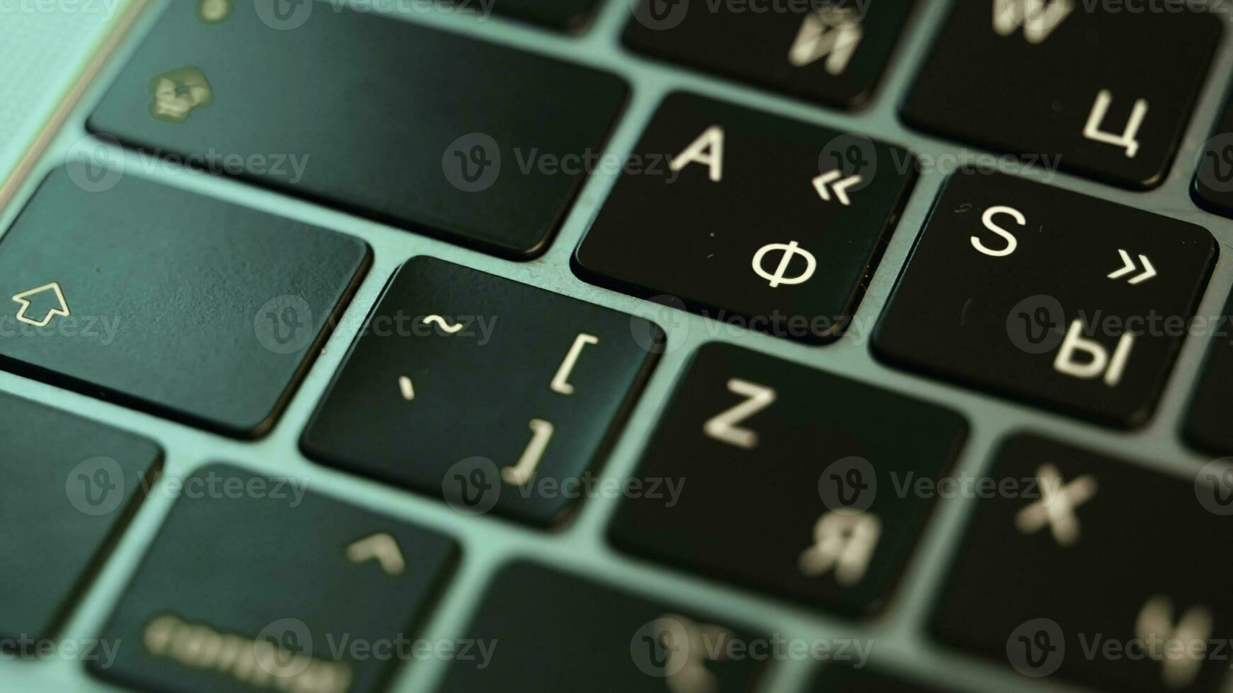 Close up of laptop or computer keyboard. Action. Concept of modern devices and technologies, buttons of a black keyboard under the green light. photo