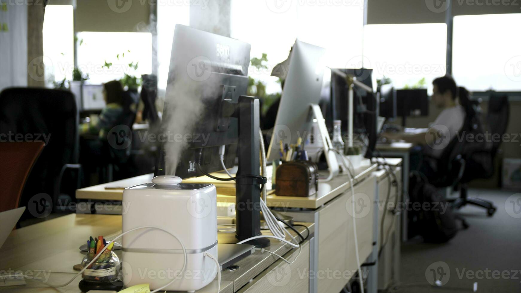 Working humidifier on the background of young people working in the office. Healthy working environment in the office. Vapor from humidifier photo