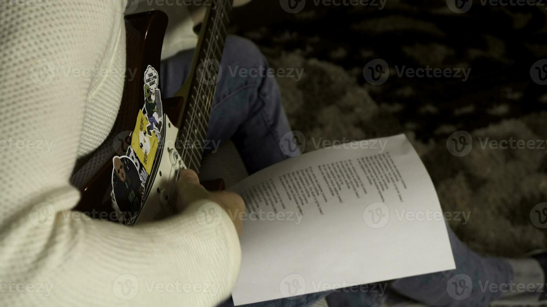 músico jugando eléctrico guitarra y mirando a papel con impreso canción palabras acostado en su rodilla. hombre guitarrista en creando canción proceso. foto