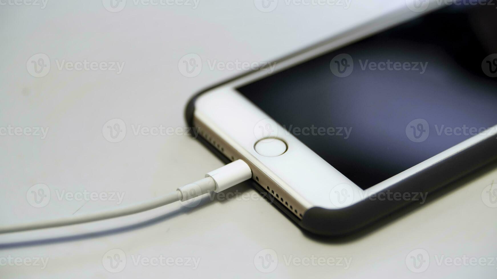 Close up of the apple iphone with the charging cable lying on the white table. Media. Process of charging of a modern device connected to usb cable. photo