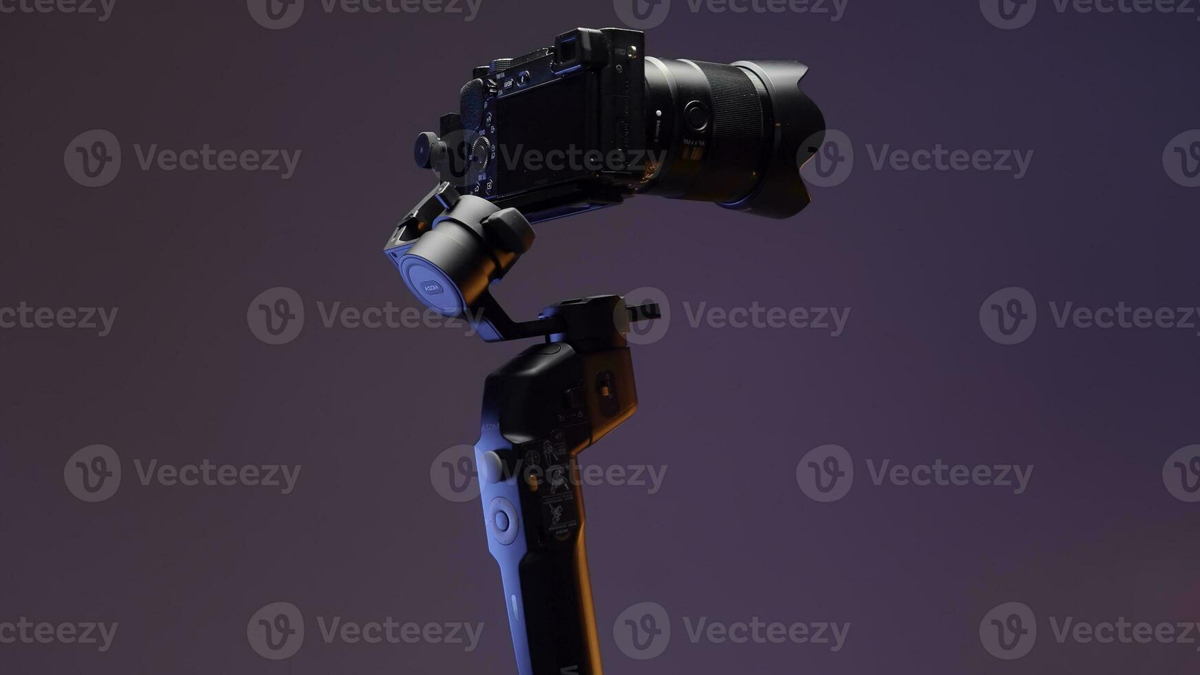 The concept of shooting with gadgets. Action.A large swivel tripod on which a large video camera is attached shoots in different directions on a bright purple background. photo