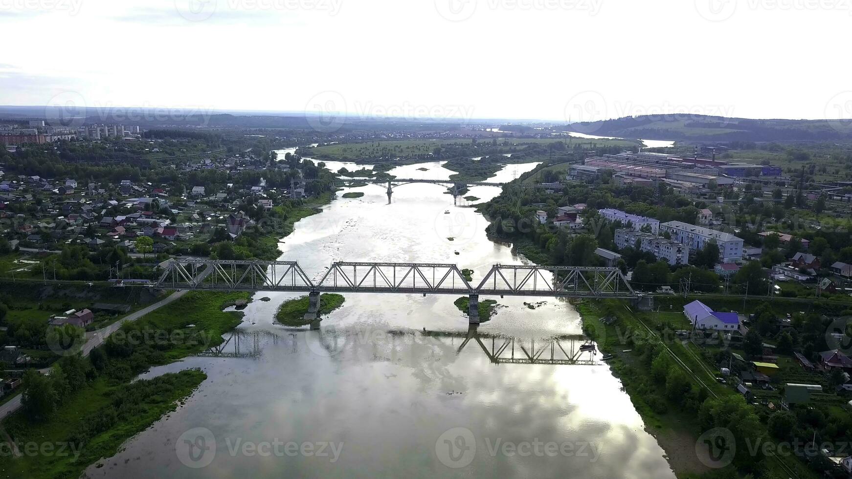 Beautiful view from the helicopter. Clip. View of the river over which there are bridges , next to the river there are residential buildings, green mountains and a bright white sky are visible photo