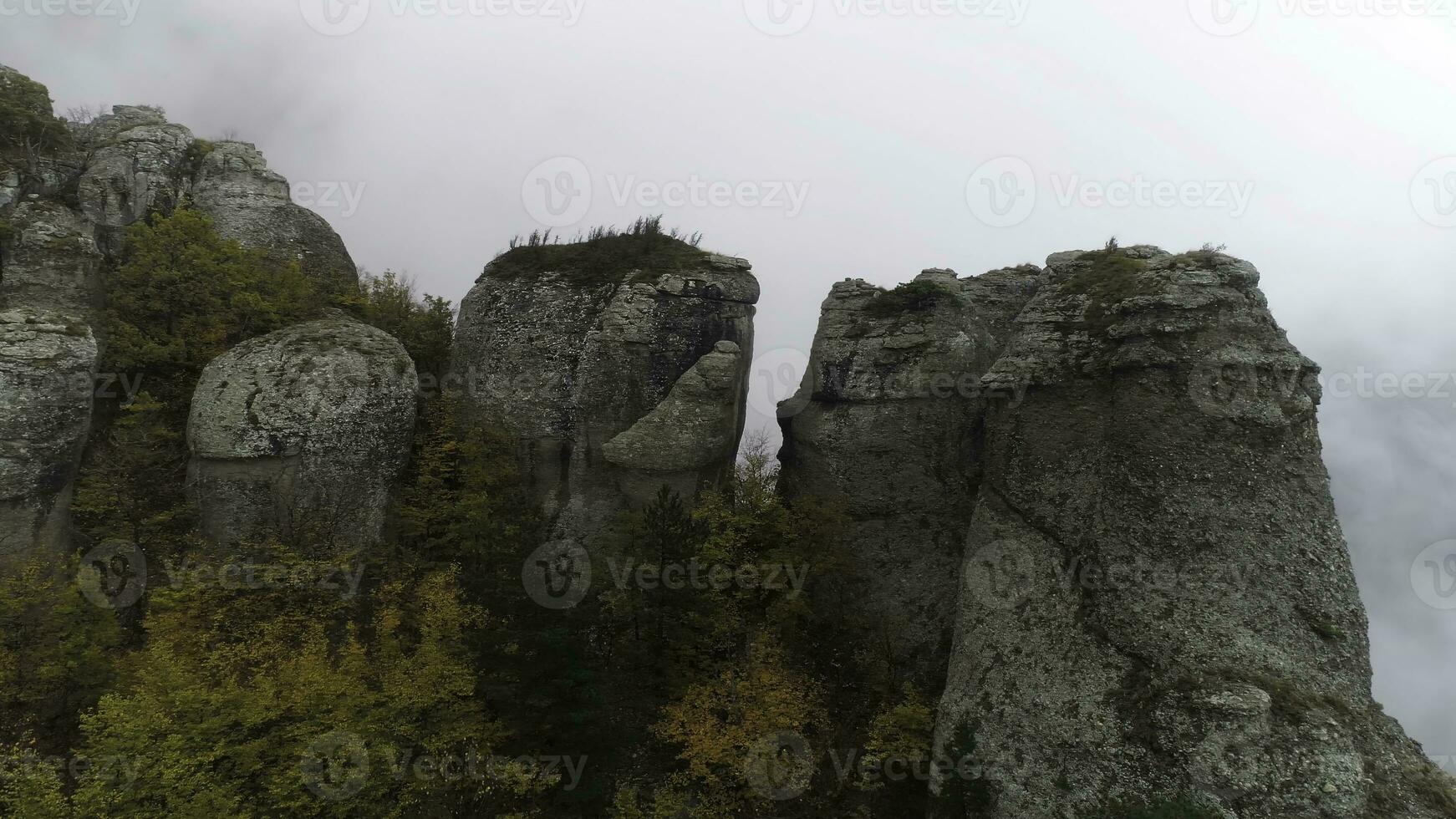 View near stone pillar of cliff. Shot. Top view of stone pillar of rock with approaching thick fog. Autumn landscape with colorful shrubs and dense gray fog on mountain photo