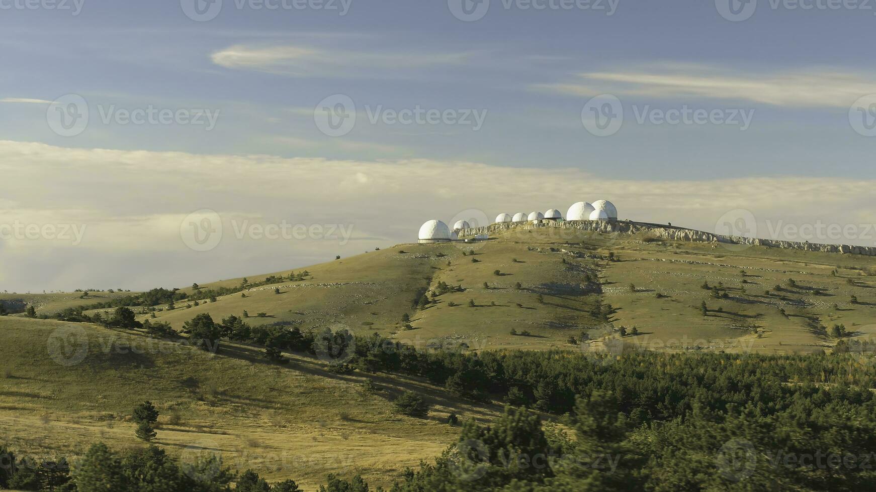 Top view of white domed buildings of observatories on hill. Shot. Astronomical research facilities and large observatories located at top with beautiful sunset sky and clouds photo