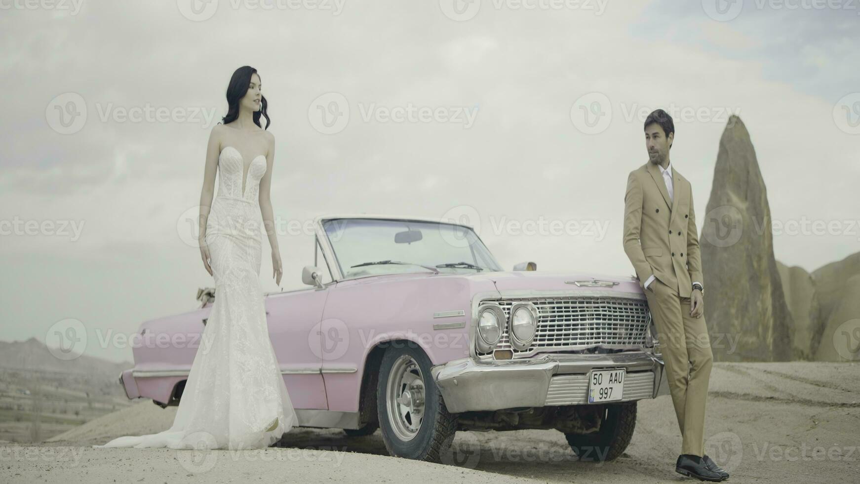 Beautiful outdoor shot next to a pink car. Action. An elegant couple with a brunette girl in a white dress and a man in a suit are walking in front of a pink car. photo