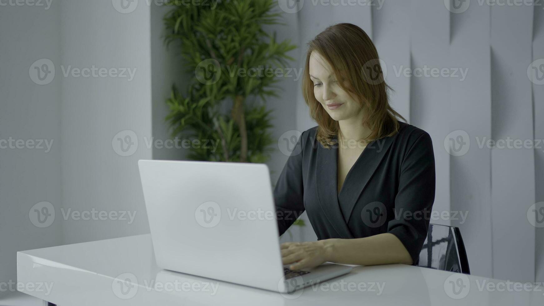 A woman working at a computer. Action.A striking woman with short hair sits at a white computer and works at a desk in black clothes. photo