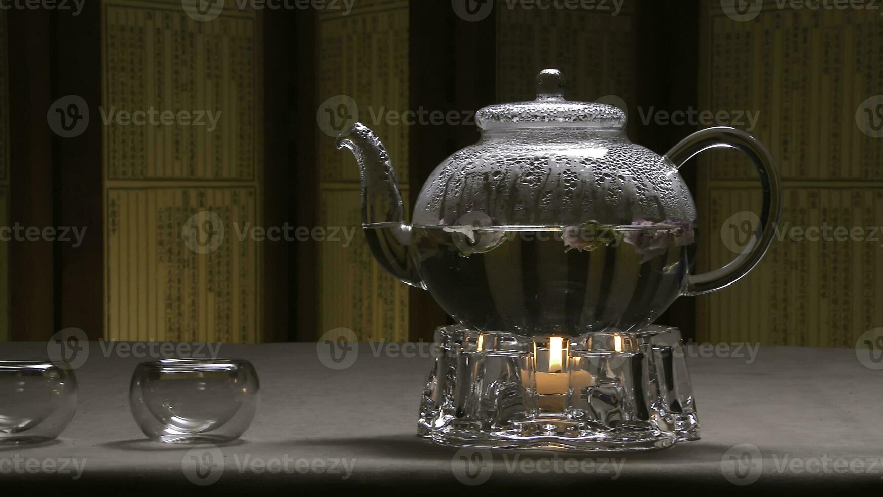 Beautiful warm picture of transparent teapot kettle with tasty green black tea on a table with candles. Glass kettle with blooming flower tea on wooden table. Stand with little candle. Chinese tea photo