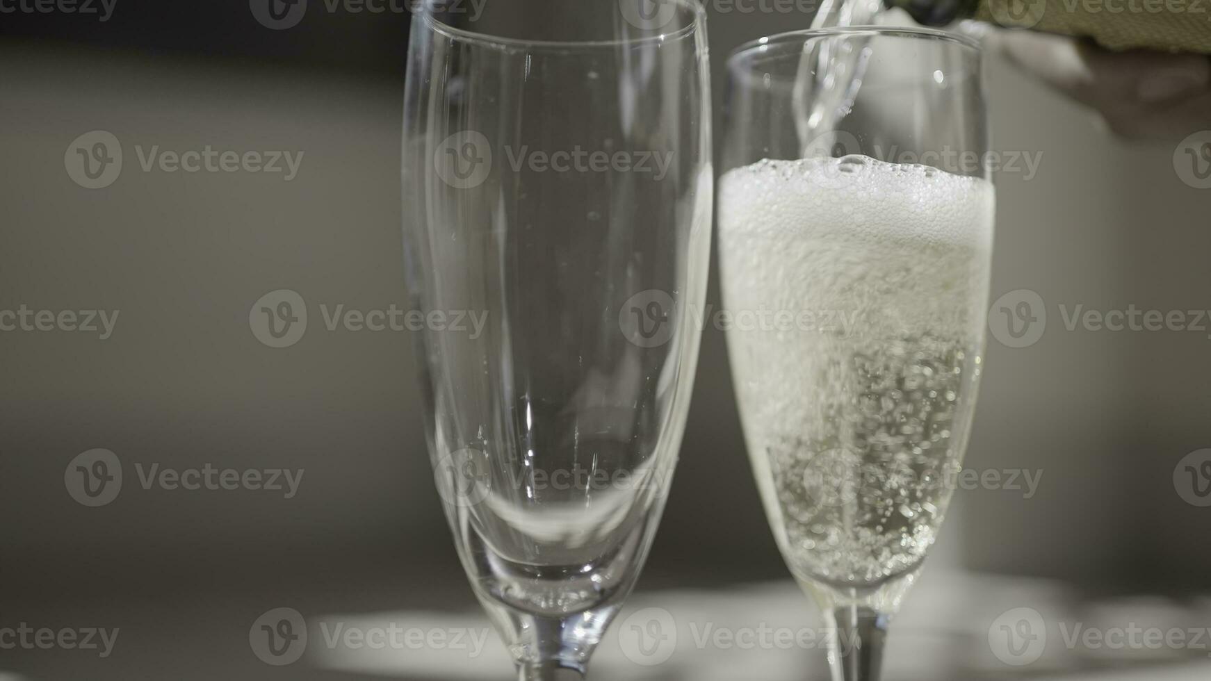 Close-up of pouring champagne into elegant wine glasses. Action. Transparent champagne glasses for date. Pouring champagne by glass on sunny day photo