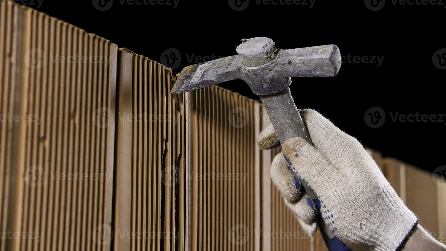 Close up of man hands holding hammer and using it to make an oblong hole on black background. Stock footage. Construction worker demolishing hole at brick wall with a hammer. photo