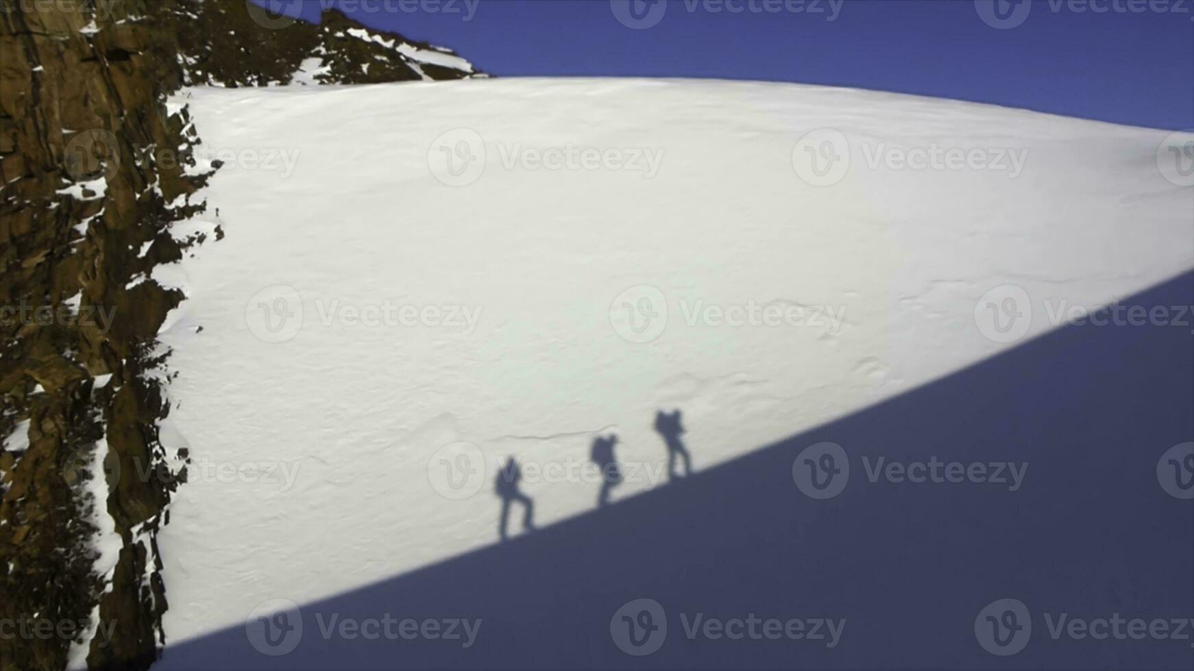 The person's shadow on a vertical cliff face. Silhouette of people climbing on overhanging cliff high above clouds and mountains, sun, beautiful colorful sky and clouds behind photo