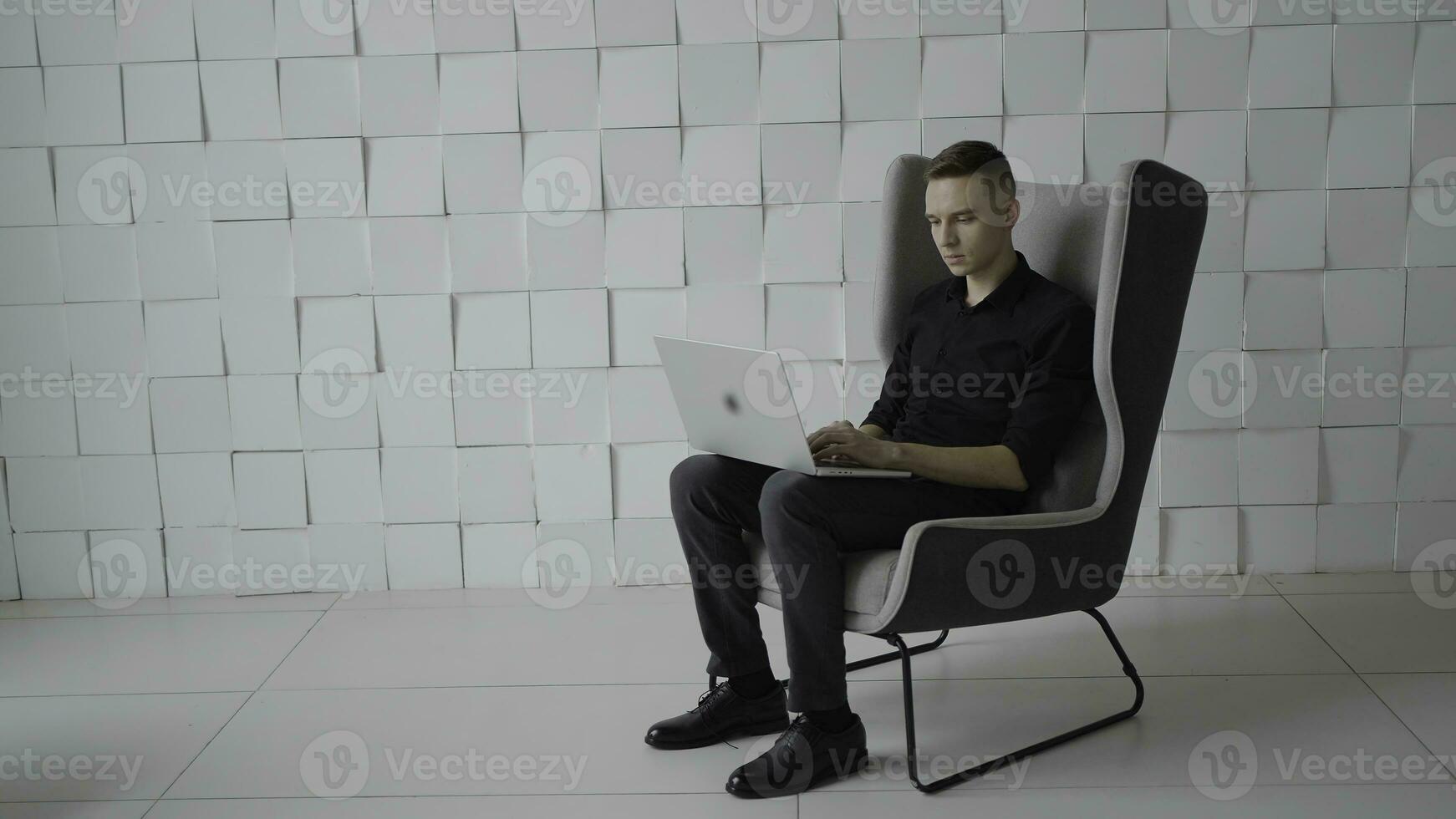 Young successful man in chair with laptop. Action. Young guy is working on laptop in business atmosphere. Business style chairs and rooms with successful man photo