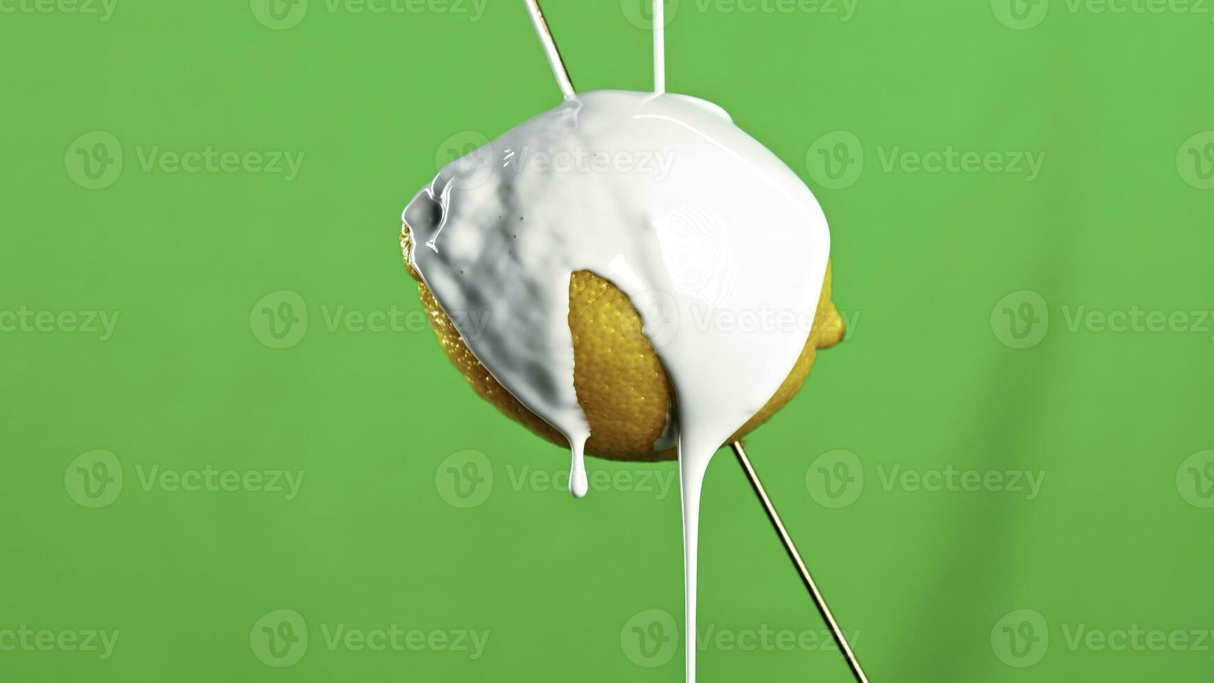 Modern art concept. Stock clip. Close up of lemon fruit on a wooden skewer being poured by white liquid paint isolated on a green wall background. photo