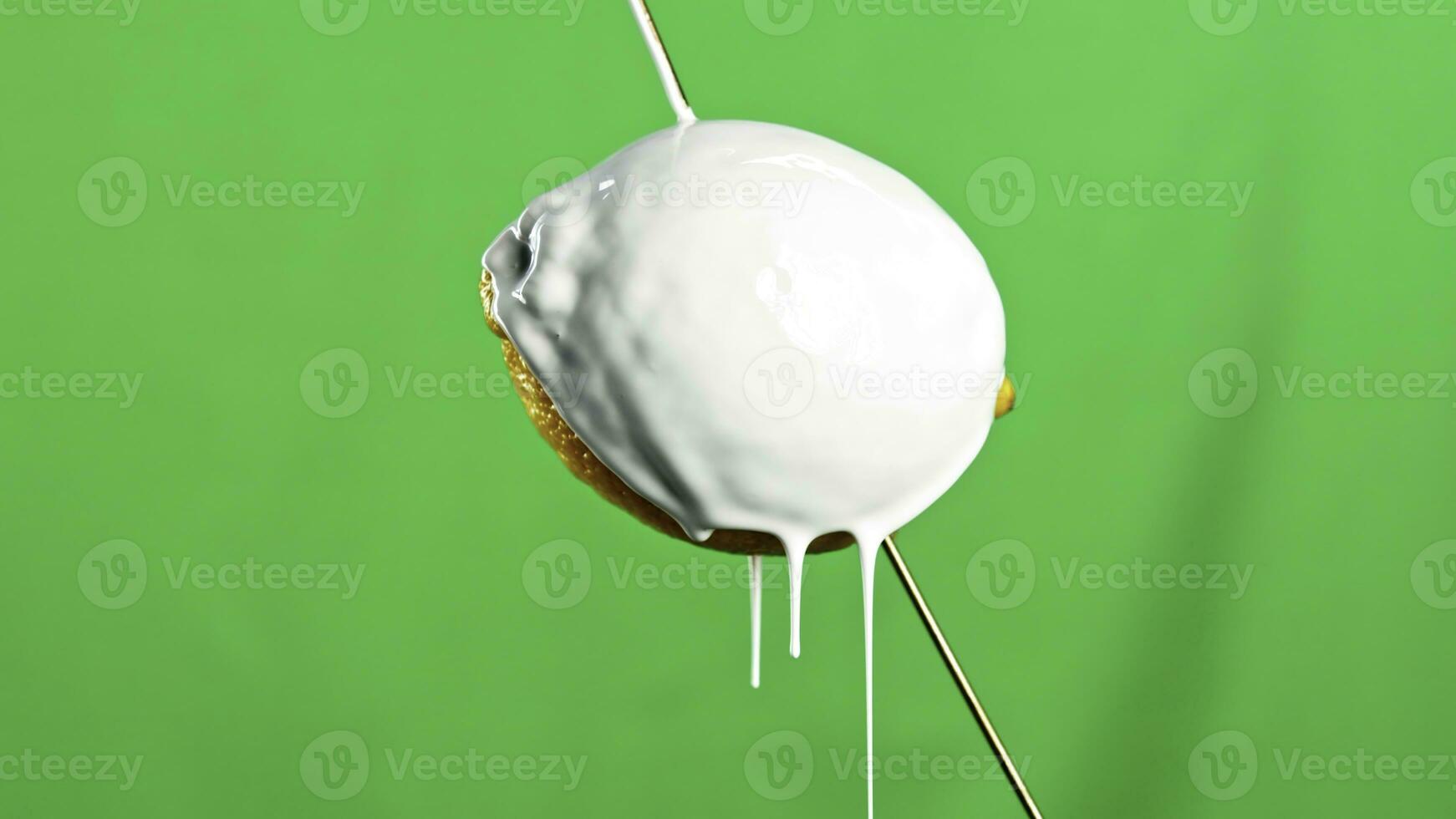 Modern art concept. Stock clip. Close up of lemon fruit on a wooden skewer being poured by white liquid paint isolated on a green wall background. photo