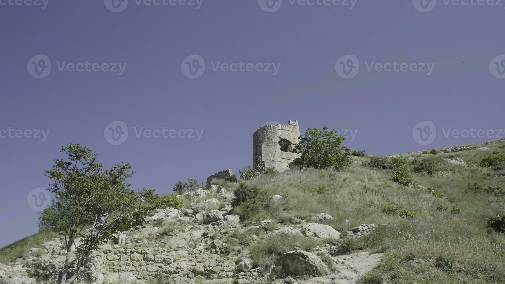 Ancient ruined castle on the top of the hill on blue clear sky background. Action. Broken abandoned stone building on green field. photo