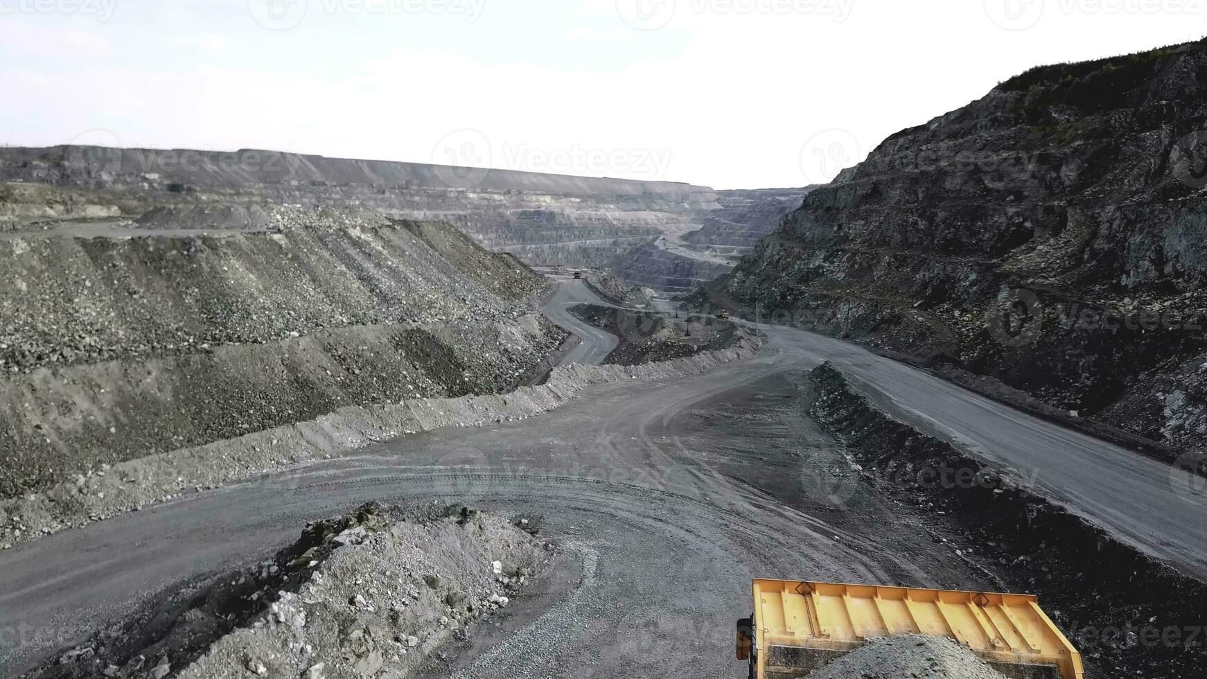 Dump truck is at quarry. Top view of driving orange dump truck with rubble on road open pit. Heavy transport in mining industry photo
