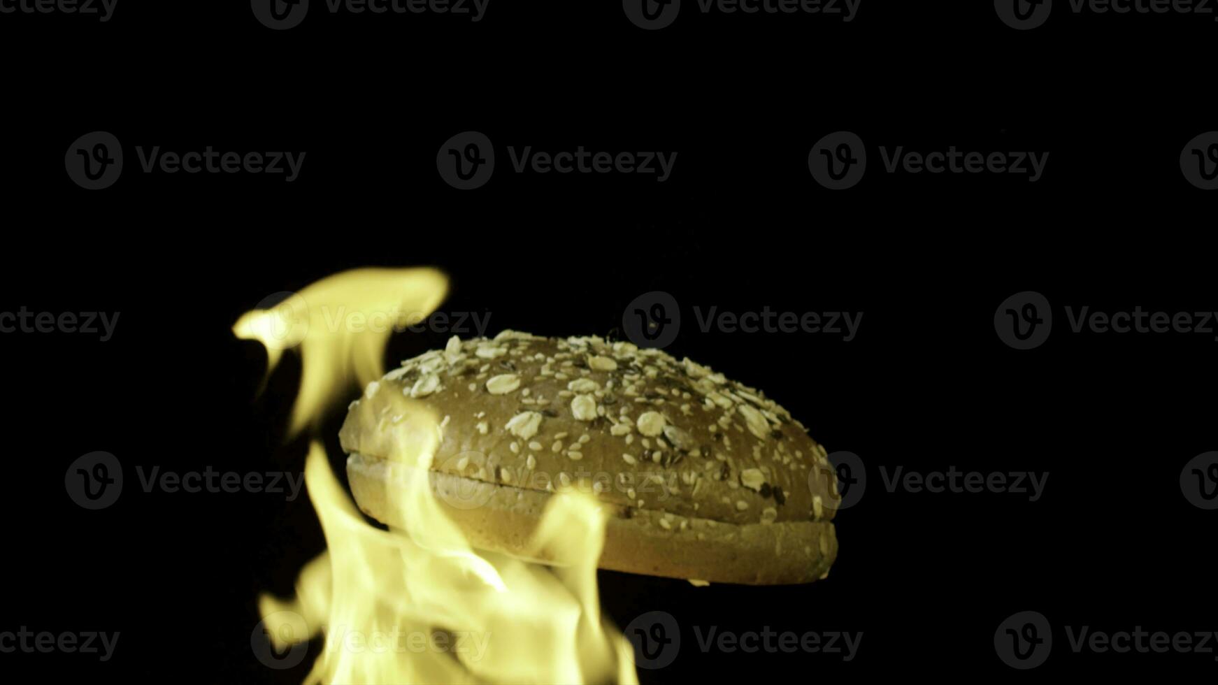 An appetizing burger bun with sesame seeds isolated on black background with red flame. Stock footage. Food and cooking concepr, rotating baked bun in flame. photo