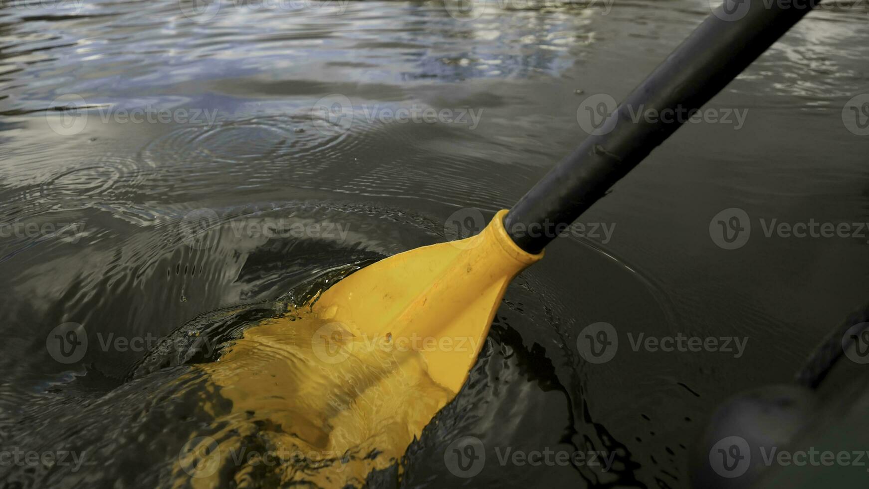 Close up of a man on a river in a green rubber boat with a yellow paddle. Stock footage. Male rowing with an oar sitting in a rubber boat. photo