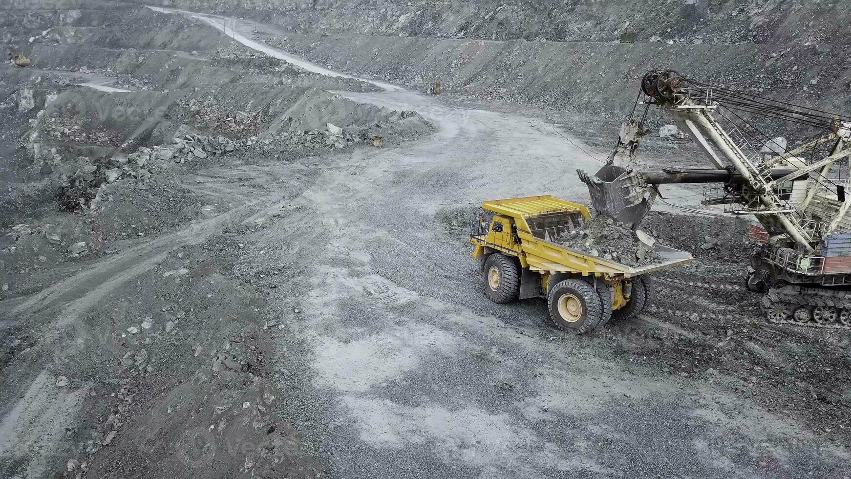 Top view of excavator in open pit. Excavator falls asleep rubble in dumper on outdoor quarry in extraction of minerals. Concept of extraction of minerals photo