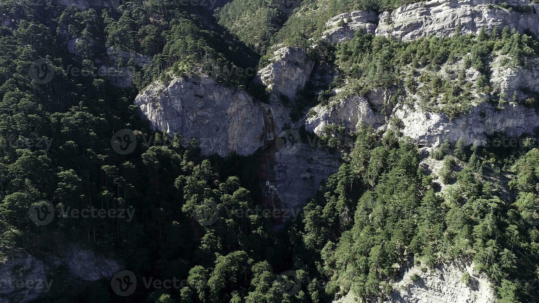 Camera moving away from the forested slope with rocks on a sunny summer day. Shot. Aerial of many green spruce trees growing on a steep mountain slope, beautiful background. photo
