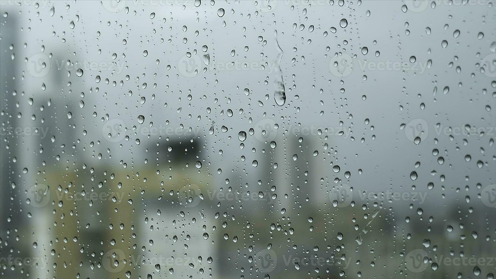 cerca arriba de un vaso ventana en un lluvioso día con grande gotas en borroso ciudad ang gris pesado cielo antecedentes. valores imágenes. transparente agua gotas en un vertical vaso superficie. foto