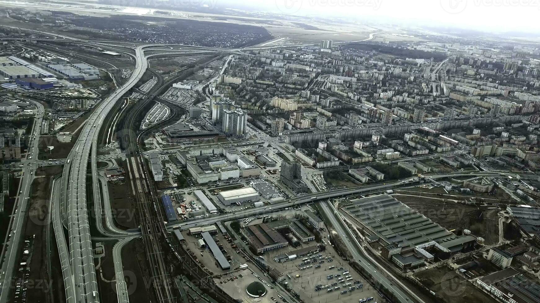 Top view of gray metropolis. Panorama of big city with areas and passing long highway in cloudy weather. Suburban industrial part of city on background of residential districts photo