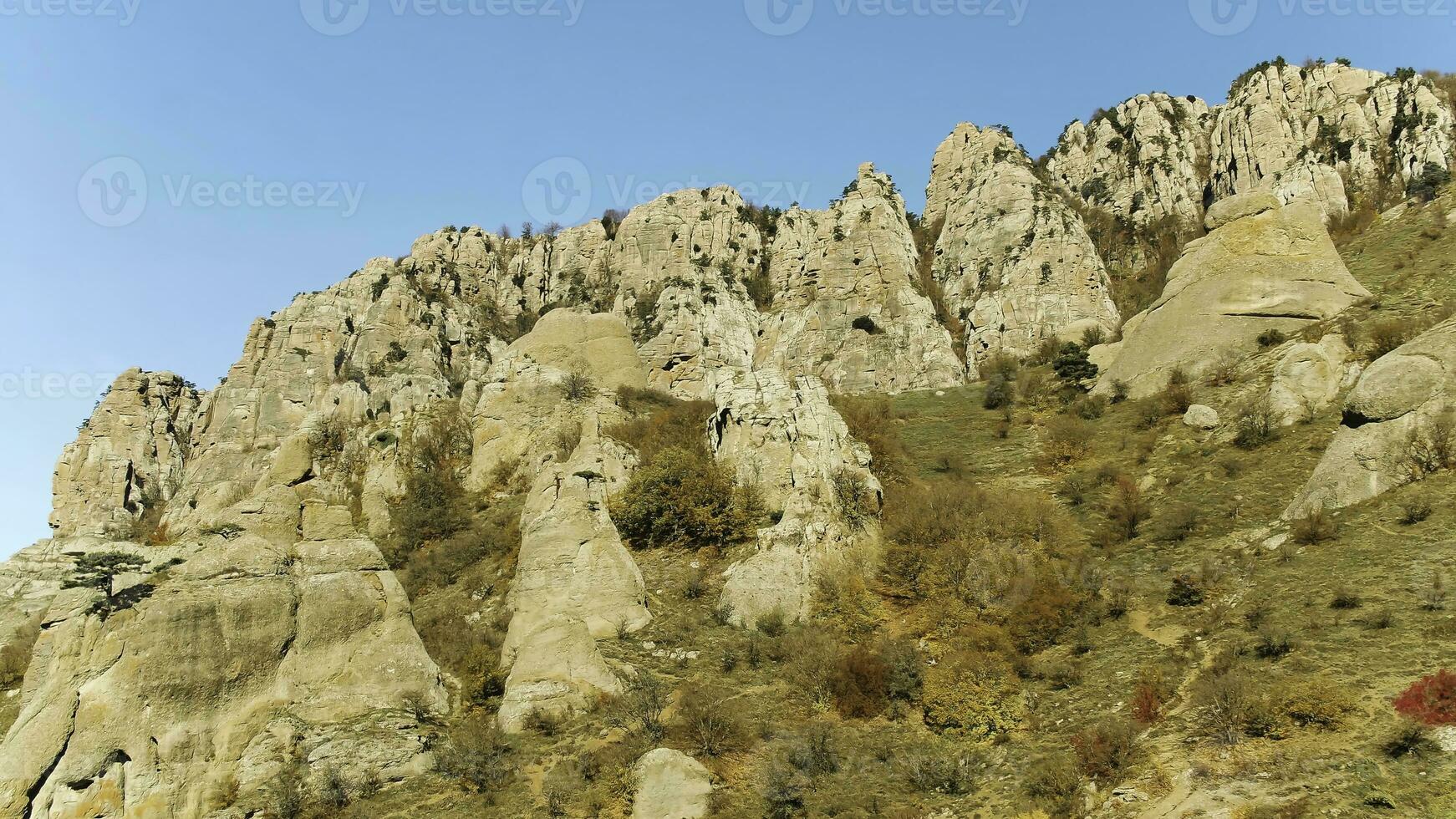 Top view of high mountain range in colorful autumn with green yellow meadows and rocky mountain peaks. Shot. View of rocky terrain of mountains. Magnificent mountain scenery against clear blue sky photo