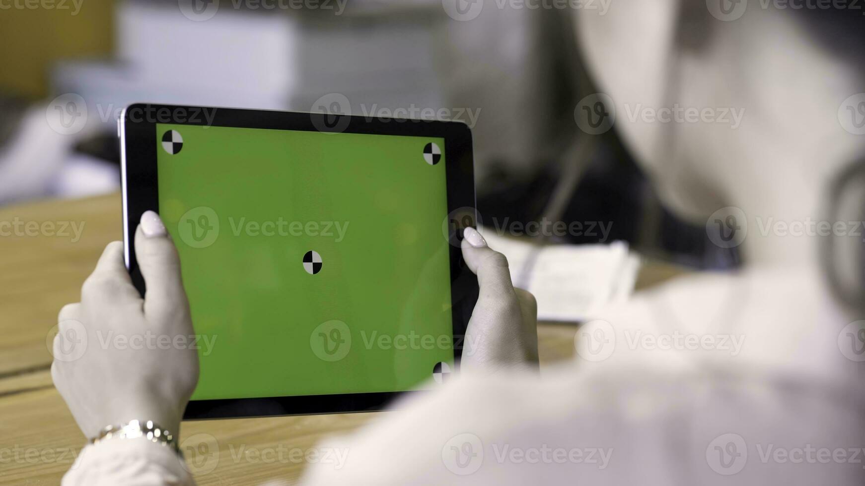 Rear view of a woman holding a tablet with chromakey with tracking marks on wooden table background. Stock footage. Different action with the device in daylight indoor space, green screen. photo