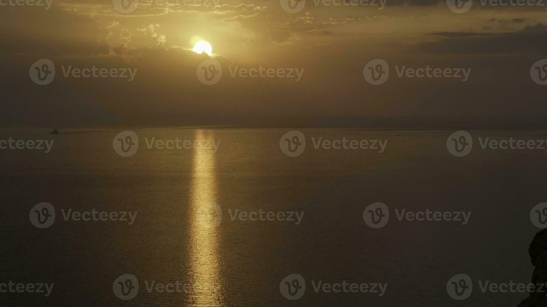 Breathtaking sunset over the Atlantic ocean with the bright golden sun coming down to the horizon. Shot. Aerial of the calm ocean, black cliff, and bronze sunset. photo