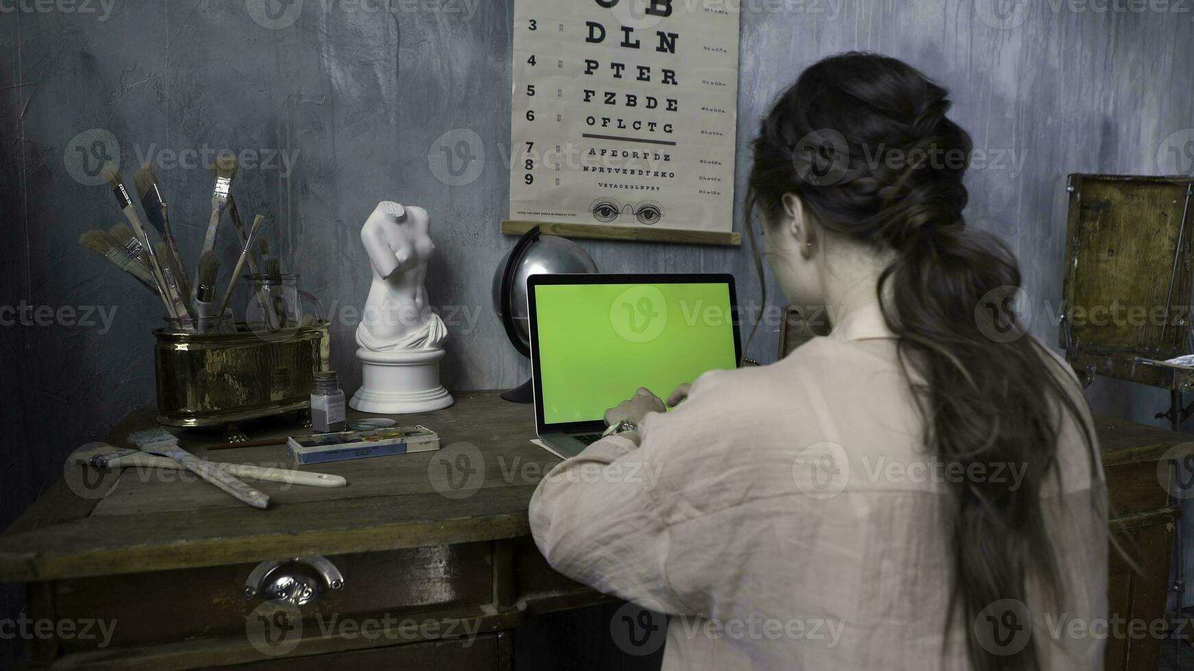 Over the shoulder shot of a woman typing on a computer laptop with a chromakey green screen. Stock footage. Woman hands typing on laptop with green screen in the artist workshop. photo