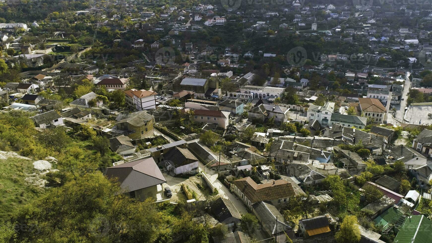 Top view of city located in valley with hills. Shot. Life in city, located between the wooded hills like resort. Summer, sun, greenery and resort town with forest and hills photo