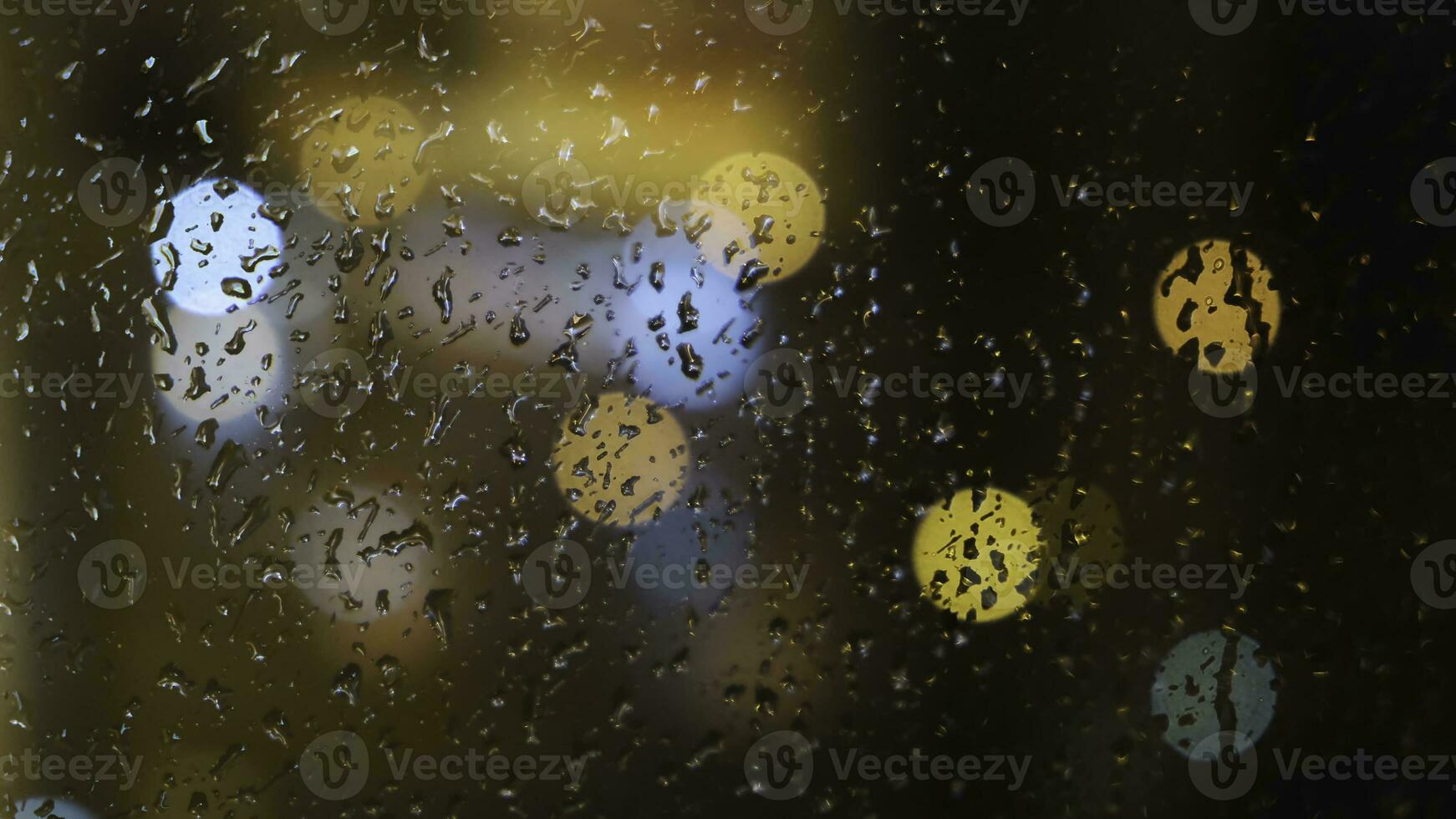 Close-up of the blurred light spots through the window and raindrops falling down on the glass at the evening. Concept. Rainy weather photo