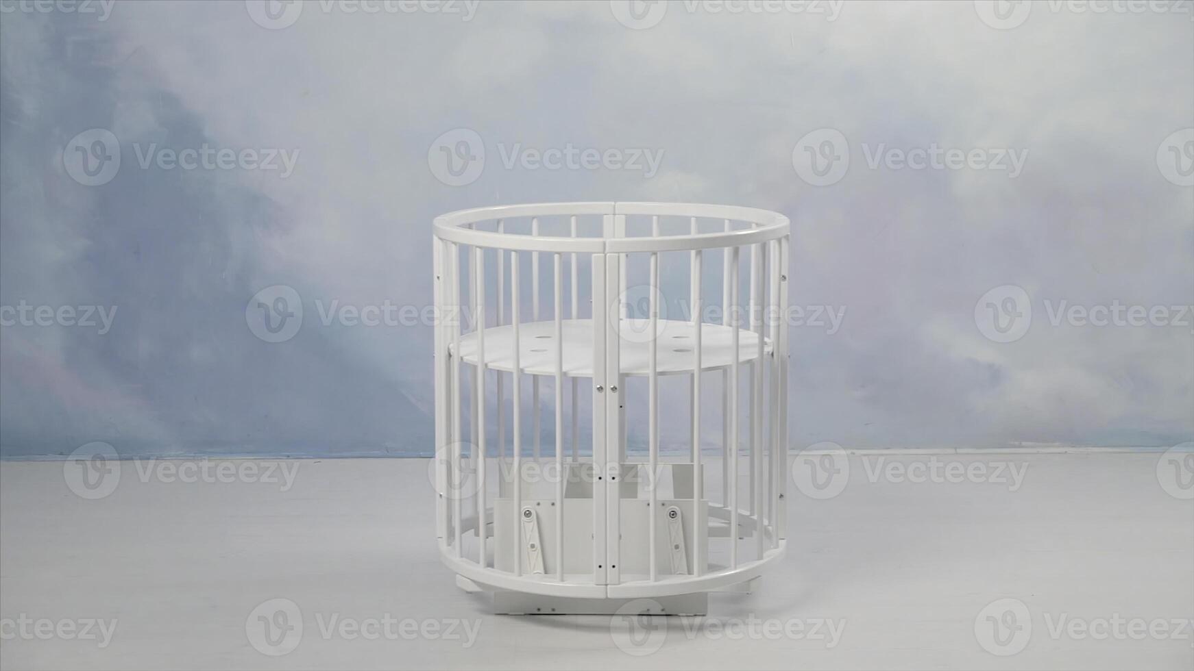 Baby white cradle swinging in the empty room in front of a wall coloured in light blue. Stock. White small baby bed swinging from one side to another in light empty room. photo